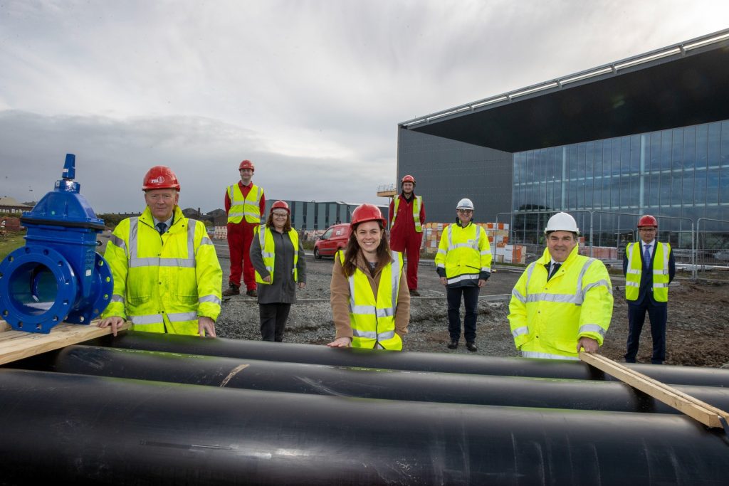 Scottish Government Cabinet Secretary for Finance and the Economy Kate Forbes in front of the heating network building along with other staff members, with the heating system pipes.