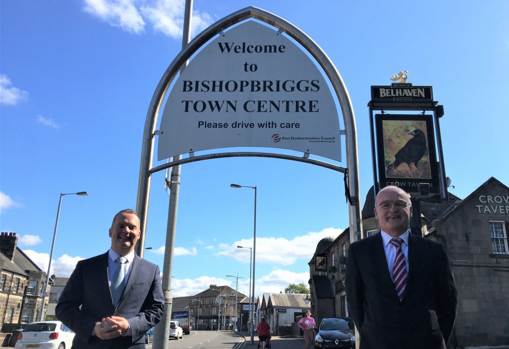 Photo of Bishopbriggs Town Centre sign with Joint Leaders Cllr Andrew Polson (left) and Cllr Vaughan Moody (right).
