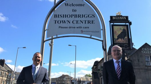 Photo of Bishopbriggs Town Centre sign with Joint Leaders Cllr Andrew Polson (left) and Cllr Vaughan Moody (right).