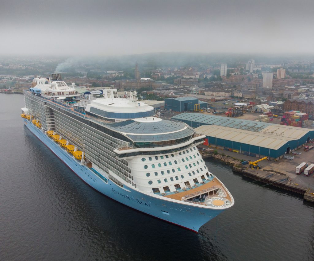 An aerial photograph of a cruise ship from above the front of the ship, showing the full cruise ship berthed at Greenock Ocean Terminal. You can see the Ocean Terminal and - stretching out behind - Greenock, behind the cruise ship.
