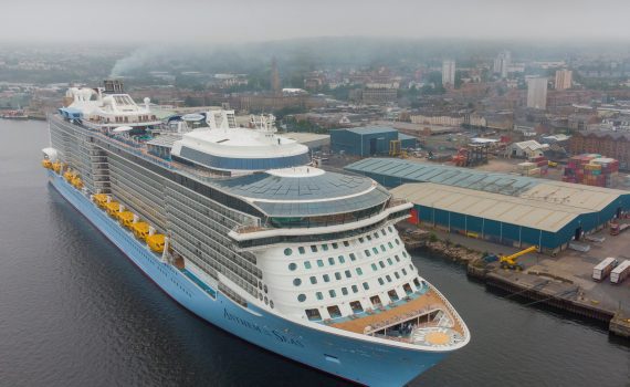 An aerial photograph of a cruise ship from above the front of the ship, showing the full cruise ship berthed at Greenock Ocean Terminal. You can see the Ocean Terminal and - stretching out behind - Greenock, behind the cruise ship.