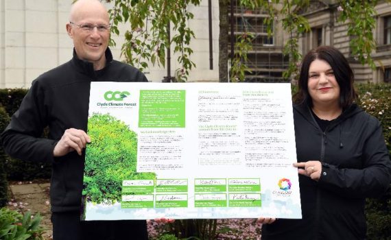 Max Hislop, director of Clyde Climate Forest, and Councillor Susan Aitken stand side by side holding the Clyde Climate Forest concordat signed by all eight council leaders.
