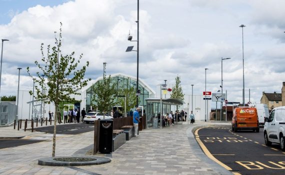 Motherwell transport interchange showing the new glass station front in the background, wide pedestrian footpaths, with trees, outside the station as well as a bus stop.