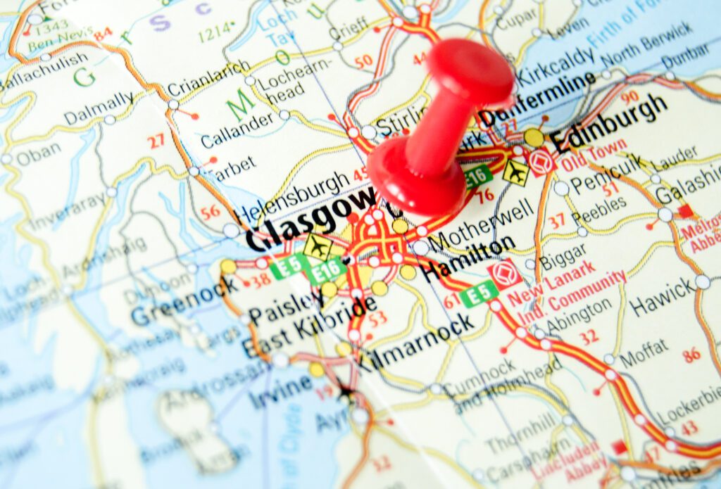 Close up photograph of a map of southern Scotland with a red push-pin in the location of Glasgow.